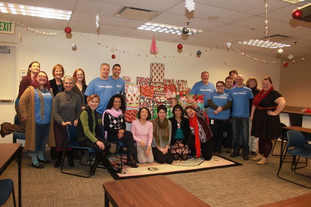 Members of Wizards of the Coast (blue shirts) and the King County Sexual Assault Resource Center pose with the company's donation of gifts to an anonymous family.