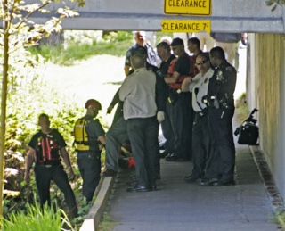 Officers from Kent and Tukwila Fire departments and Tukwila Police Department huddle underneath the Strander Boulevard bridge on the banks of the Green River after the Kent Fire Boat retrieved the body from the water.